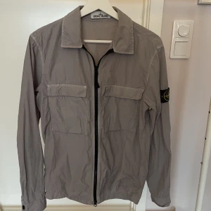 Stone Island jacka strl S - As snygg Stone Island jacka/överskjorta i grå, herrstorlek S. Perfekt vår och sommarjacka! Fint skick, nypris 3100kr, säljs för 1800kr. Köpt på NK i Göteborg, kvitto finns!