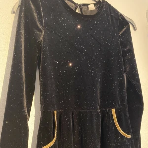 Svart festklänning barn - Vacker svart festklänning med guldglitter på i mjuk stretch tyg. Används 2 ggr och är som ny. 