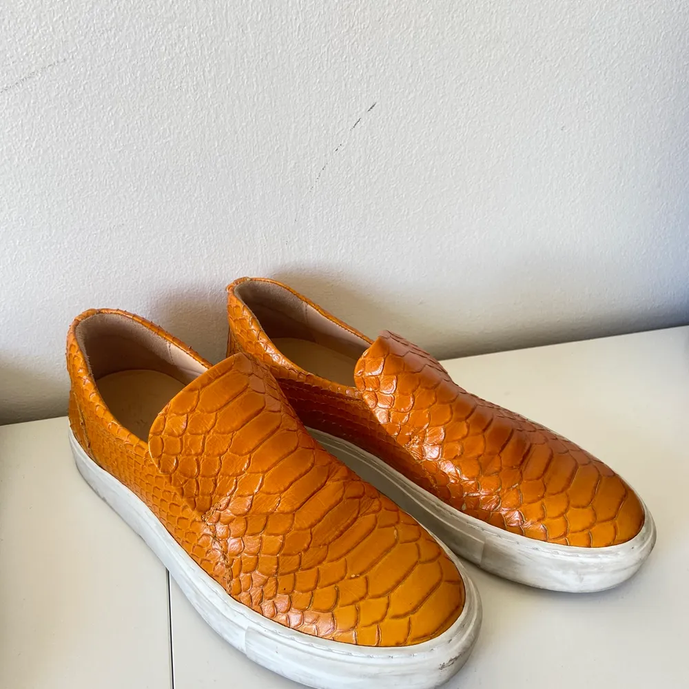 Slip ons från Billi Bi. Organgea med krokodilskinns mönstrat äkta läder. Använda några gånger och därav är den vita kanten runt om skon smutsig, annars i topp skick. . Skor.