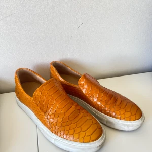 Billi Bi slip ons - Slip ons från Billi Bi. Organgea med krokodilskinns mönstrat äkta läder. Använda några gånger och därav är den vita kanten runt om skon smutsig, annars i topp skick. 