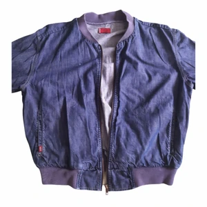 Levi's Bomberjacka i Denim - En mycket fin jomberjacka i mörkt tunnt jeans tyg av märket LEVI'S. Jackan har en stickad mudd runt nacke, vrist och midja i en dov lila färg. Köpt begagnad och använd några gånger. Mycket fint skick men 7 små röda färgfläckar på höger arm se bild. Buda!!