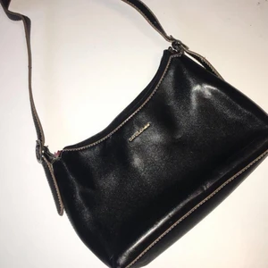 Liten svart handväska från David Jones - Liten svart handväska från David Jones med söta beige-bruna detaljer. Den är köpt second hand men aldrig använd av mig då det inte är min stil. Den är i fint skick!👜