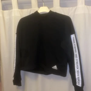 Collegetröja  - Collegetröja med lite polokrage. Text på båda armarna och adidas loggan nere på vänster sida. Kan användas till träning eller vardag! 