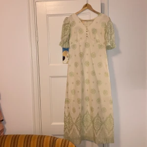 Söt 70-talsklänning - 70-talsklänning i vitt och grönt med guldiga knappar. Producerad i Sverige. Storlek 38 🌸 säljer billigt pga flytt och har för många 70-talsklänningar!