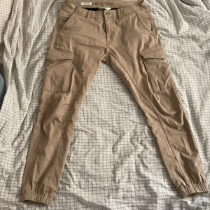 Beige jack and jones cargobyxor - Knappt använda. Beiga cargobraller från Jack and Jones, köpta i affär för 500kr, modellen heter Tapered/Paul. Materialet är stretchy 