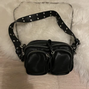 Väska från Gina Tricot  - Svart väska i fint skick från Gina Tricot. 4 ytterfack varav ett har ett litet fack inuti. Kan litet svart band (axelremsband) och längre kedja finns med.