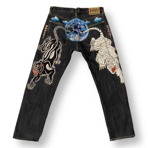 Sugoi Jeans  - Coola jeans med broderi på baksidan. 100% bomull. Storlek 34, liten i storlek - kolla mått. Midjebredd 42cm, grendjup 28cm, höftbredd 56cm och innerbenslängd 78cm. 