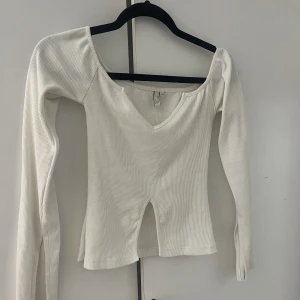 Of shoulder top - Storlek: XS En vit of shoulder topp med en liten slits på magen och även slits vid slutändan på armarna. Toppen är från Nelly och är knappast använd. Köparen står på frakten😊
