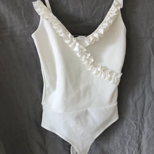 VitBeige Body med volang stl XS - VitBeige body med fina detaljer🩱volang och smala axelband. Gina Tricot stl XS. Passar till byxor, shorts och kjol.