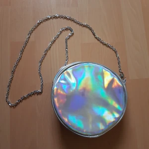 Holografisk väska - Jättesöt holografisk liten axelväska i rund form, med silverkedja som band. Rymlig, ca 18 cm i diameter.
