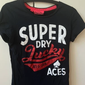 Superdry T-shirt  - Denna snygga superdry T-shirt säljs nu för att den tyvärr inte längre kommer till användning. Den är svart med vit text. Samt att den röda texten är i glitter. Skriv för mer bilder 😊