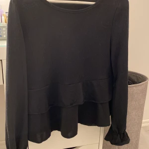 Svart volang tröja  - Svart topp/tröja med volang i ärmarna och i midjan. Oanvänd och jättegullig. Litee kort i ärmarna på mig men det är inget jag stör mig på. 60kr+frakt