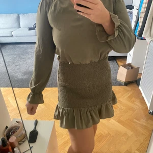 Grön/brun klänning  - Stilig och klassisk klänning i brun/grön kulör. Smock nertill och mer blusaktig upptill. Ej använd. 