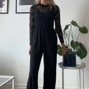 Byxdress/jumpsuit - Oanvänd svart byxdress med prislapp kvar. Storlek S. Fina spetsdetaljer i ryggen. Ordinarie pris 499kr.