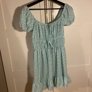 Sommarklänning - Kort sommarklänning från ASOS, i grönt blommigt mönster, två knytdetaljer framtill. Går att ha som off shoulder och med söta puffiga axlar. Aldrig använd. Nypris 399kr. Frakt tillkommer!!!