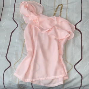 Volang rosa topp - En jättesnygg rosa topp som jag säljer då den inte går på mig. Är jättefin och man kan ha den på olika evenemang. Har en guldkedja vid ena axeln som är så fin. Denna topp har gett mig många komplimanger. Storlek XS. Köparen står för frakten ❤️