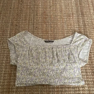 Sommartröja - Säljer denna jättegulliga korta sommartröjan. Den är vit med små lila blommor och du kan själv välja om du vill ha den off shoulders eller som en vanlig t-shirt. Knappt använd ❤️