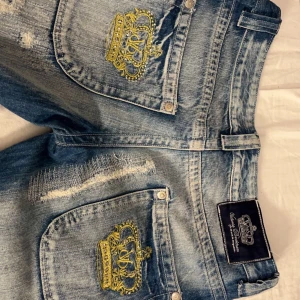Lågmidjade jeans  - Säljer dessa Victoria Beckham jeans med guldiga kronor på bakfickorna och lite slitningar! Dom är lågmidjade och köpta här på plick men säljer då jag inte tyckte dom passa mig så bra, dom är uppsprättade längst ner på benen så dom ska passa mig som är 168