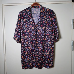 Blommig blus - Blommig vintageblus med svart botten. Knäpps med knappar. Ingen storleksmärkning men är som en L🌿