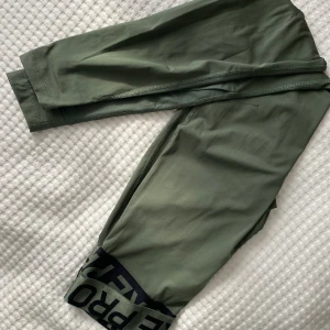 Gröna träningstights från Nike - Ett par gröna träningstights från Nike. Öppna vid vaderna. Nikemärket har suddats bort men annars är de jättesnygga!