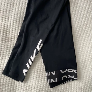 Träningstights från Nike - Svarta träningsbyxor från Nike med detaljer längs smalbenen och runt midjan. Använda ett par gånger och är i gott skick! Jag har klippt av lappen som sitter i byxorna då den gav skavsår.