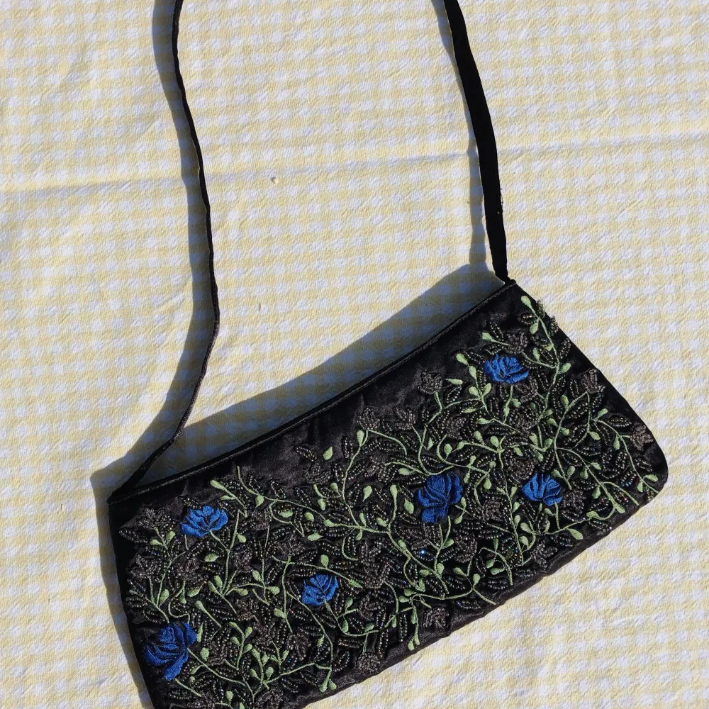 En liten svart handväska i sidenliknande tyg med pärlbroderier.. Väskor.