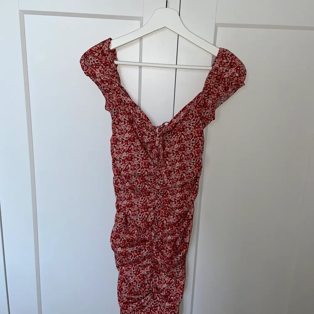 Blommig röd klänning med scrunch både fram och bak för en kroppsformad figur. Detalj vid bysten med rosett.  Använd en gång.. Klänningar.