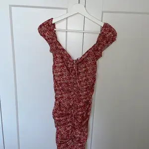 Blommig röd klänning med scrunch både fram och bak för en kroppsformad figur. Detalj vid bysten med rosett.  Använd en gång.