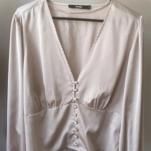 Festtopp - Supersöt ljusrosa festtopp i siden material. Den är v-ringad med knappar och har resår i ryggen. Lite kortare topp med långa, lite puffiga ärmar.   Köparen står för frakten!