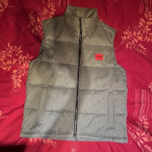 Hugo väst grå - Hej! Säljer en fin HUGO väst med ett tygliknande material. Storlek L men passar även M. Tags finns kvar aldrig använd. Säljer eftersom jag fick den i present men den är för stor för mig.  Originalpris: 3100kr Mitt pris: 1500kr.