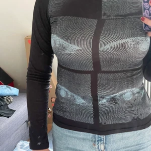 svart långärmad tröja med ögon - En svart långärmad tröja med blåa ögon, materialet är som en träningströja på ett ungefär, men väldigt cool. Stretchig och går till midjan. Baksidan har inget tryck utan är bara svart.