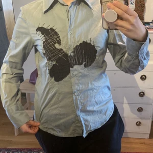 Annorlunda och snygg skjorta - Snygg ljus blå/turkos skjorta med någon sorts sjöhästsaktig tryck på både fram och baksida. Gillar den här as mycket eftersom att den har tryck och är lite annorlunda än en vanlig gammal skjorta! Snygg att ha med jeans, kostymbyxor, kjol, en snygg vaka osv! OBS: Storleken är M men skulle säga att de passar bättre som en S! 