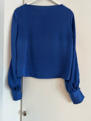 Satinblus med knappar längs ärmarna. - Jättefin blå satinblus med knappar längs ärmarna från Lindex.  Väldigt bra skick.