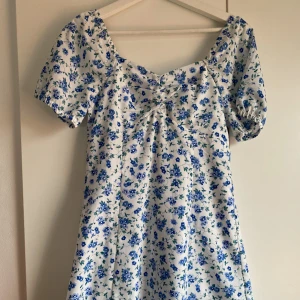 Sommarklänning - Superfin vit sommarklänning med små blå blommor på. Klänningen är aldrig använd och har prislappen kvar! 