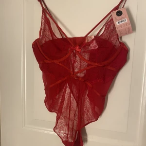 Spetsbody  - Röd spetsbody med bygel och små fina detaljer längst bysten, aldrig använd! Prislappen sitter kvar. Nypris 449 säljer den för 224kr