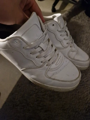 Vita låga sneakers i skinn - Klassiska vita sneakers med lågt skaft och snörning. Skorna har en stilren design med detaljerade sömmar och en tjock sula. Tillverkade i skinnliknande material och passar perfekt till streetwear eller casual outfits.