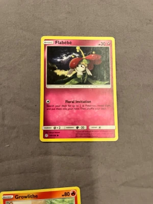 Pokémonkort Flabébé rosa - Pokémonkort med Flabébé-motivet. Kortet är rektangulärt med gul ram och har en rosa bakgrund. Text och illustration på framsidan, tillverkat i laminerad papp. Perfekt för samlare eller Pokémon-fans.