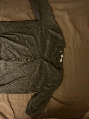 Mörkgrå kofta från Zara - Snygg mörkgrå kofta från Zara med rund halsringning och knäppning framtill. Tillverkad i mjukt material som känns skönt mot huden. Perfekt att slänga över en t-shirt eller linne för en avslappnad look.