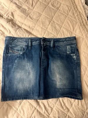 Jeanskjol - Kort fin jeanskjol från diesel. Mörkblå med ljusa detaljer. Ca 30 cm från toppen till botten. Superfin till sommaren. Säljer då den tyvärr blivit för liten. Storlek 27 skulle säga att den passar en xs/s. Den är i ett superfint skick! 