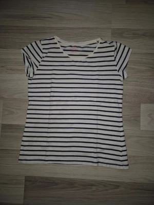 Randig vit och svart t-shirt - Klassisk t-shirt med svart och vita horisontella ränder. T-shirten har rund halsringning och korta ärmar. Perfekt för en avslappnad stil och enkel att matcha med jeans eller shorts.