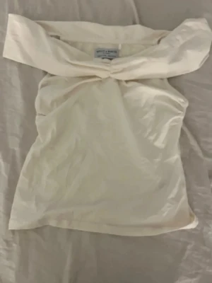 Offshoulder topp från Holly & Whyte - Använt cirka två gånger för att jag tröttnade,Snygg offshoulder topp från Holly & Whyte i ljus beige bomull. Toppen har en twistad detalj framtill och är axelbandslös, vilket ger en trendig och stilren look. Perfekt för dig som vill ha något enkelt men ändå unikt.
