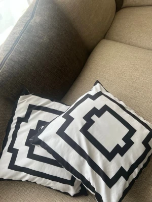Svartvita prydnadskuddar med mönster - Två prydnadskuddar med grafiskt svartvitt mönster i fyrkantig form. Kuddarna har vita bakgrunder med svarta kantiga linjer och är tillverkade i tyg. Perfekta som inredningsdetalj i soffan eller på sängen. ENDAST KUDDFODRAL ! 