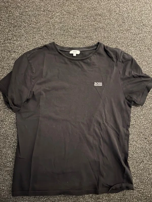 Svart t-shirt från BOSS - Snygg svart t-shirt från BOSS med diskret logga på bröstet. Klassisk rund halsringning och korta ärmar. Tillverkad i mjuk bomull som känns skön mot huden. Perfekt basplagg för en clean och stilren look.