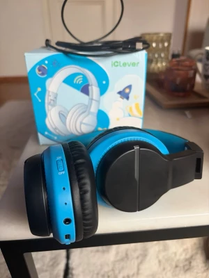 iClever blå svarta trådlösa hörlurar - Säljer ett par snygga trådlösa hörlurar från iClever i blått och svart. Over-ear-modell med vadderade kåpor och justerbart huvudband. Hörlurarna har inbyggda knappar och uttag för kabel. Perfekt för musik, gaming eller videos.