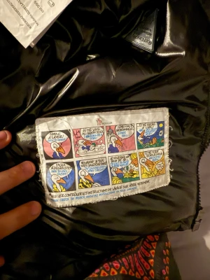 Svart pufferjacka från Moncler - Snygg svart pufferjacka från Moncler med glansig finish och klassisk logga på ärmen. Jackan har huva, quiltad design och dragkedja framtill. Kan gå ner i pris vid smidig affär 