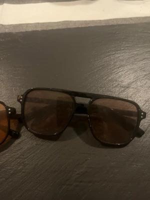 Svarta pilotbågar solglasögon - Snygga solglasögon med svarta pilotbågar och bruna glas. Klassisk retrostil med markerad näsbrygga och detaljer vid bågens hörn. Perfekta för att lyfta din look med en cool vibe.50kr styck 