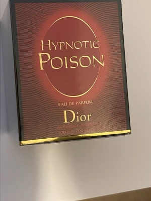 Dior Hypnotic Poison Eau de Parfum - Dior Hypnotic Poison Eau de Parfum i elegant röd och svart kartong med gulddetaljer. Doften är känd för sin intensiva och sensuella karaktär, perfekt för dig som gillar exklusiva och djupa parfymer. Flaskan rymmer 100 ml och har en lyxig design.