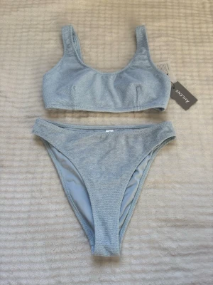 Ljusblå bikini från Åhlens - Trendig ljusblå bikini från Åhléns med sportig topp och högt skurna trosor. Bikinin har en mjuk, frottéliknande textur som ger en unik känsla och look. Perfekt för strandhäng eller poolparty. Materialet känns bekvämt och följsamt mot huden!💓🌸