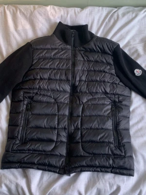 Svart pufferjacka från Moncler - Snygg svart pufferjacka från Moncler med quiltad framsida och stickade ärmar och rygg. Jackan har hög krage, två dragkedjefickor fram och Moncler-logga på ena ärmen. Perfekt för kalla vinterdagar och riktigt trendig look. Priset kan diskuteras o hör gärna av dig om du undrar nåt❤️💯