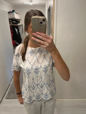 Ny vit topp med blått broderi Hampton Republic - Söt vit topp från Hampton Republic med blått broderat mönster. Kortärmad modell med vågig kant nertill och vid ärmslut. Tillverkad i tunn, luftig bomull som passar perfekt till sommaren. Storlek 40 men liten i storleken, mer som 38. 